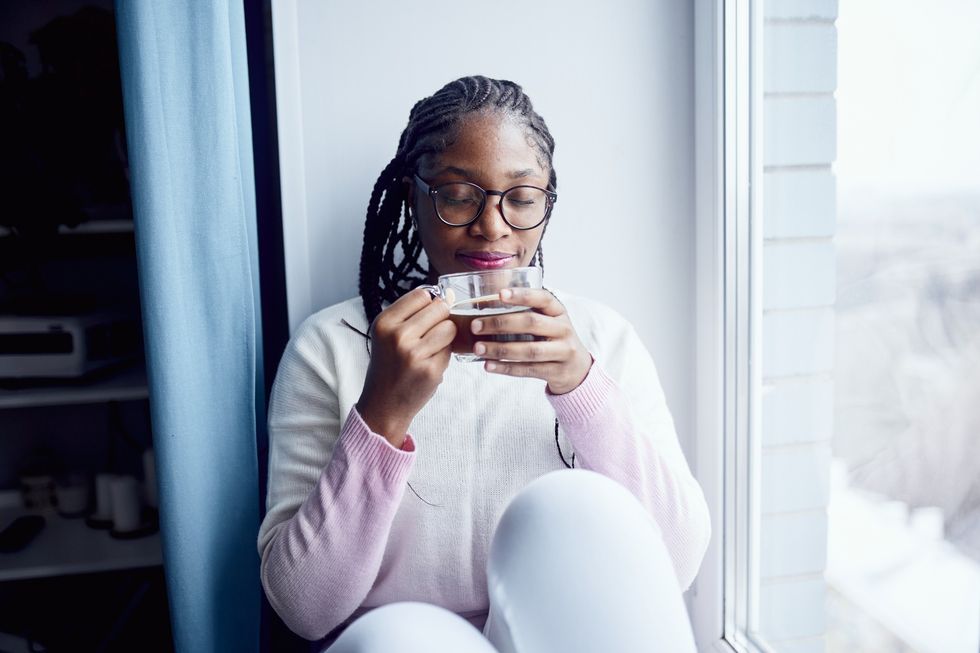 woman-wearing-glasses-sitting-in-window-sill-drinking-warm-beverage