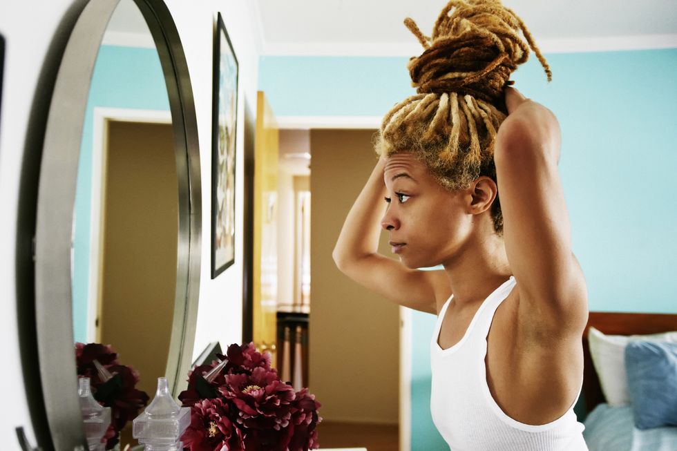 woman-wearing-tank-top-adjusting-her-blonde-locs-into-a-style-in-the-mirror