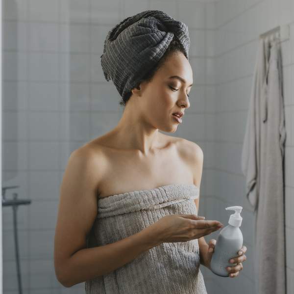 Woman Wrapped in a Towel after a Shower Holding a Skin Care Product