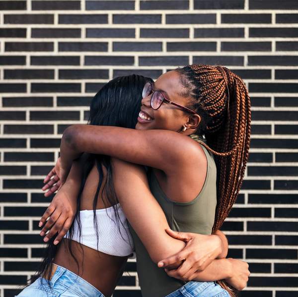 young african women smiling happy and hugging each other in front of a brick wall, concept of youth and friendship, copy space for text