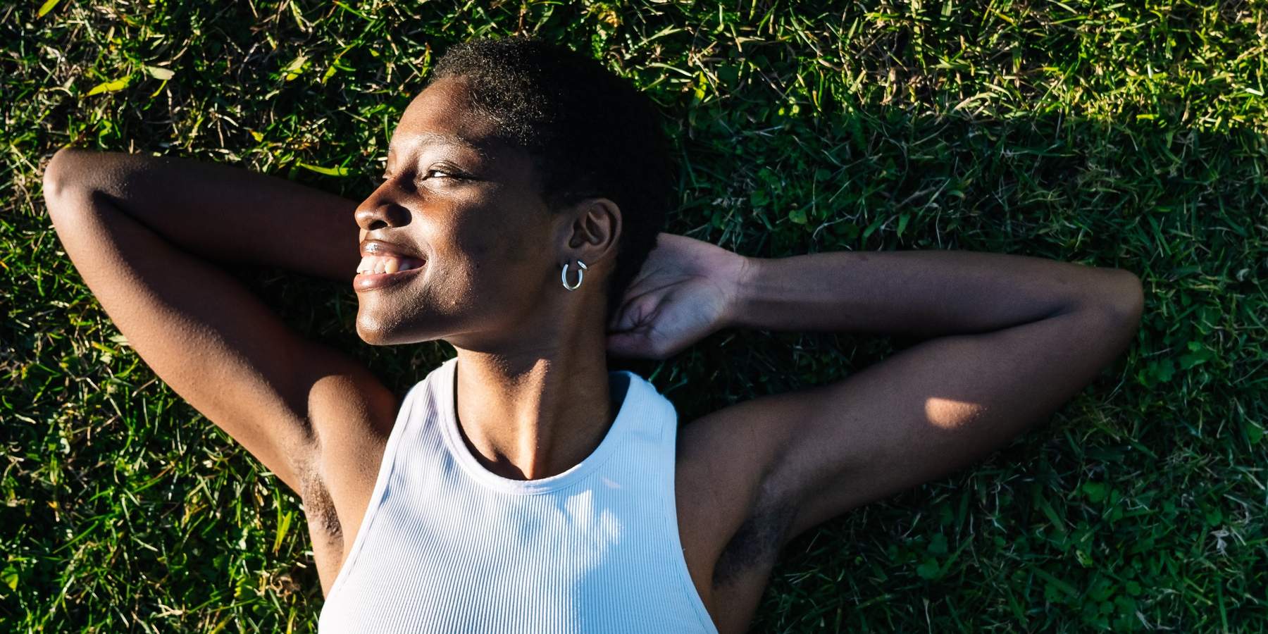 Young black woman relaxing lying on green grass smiling with hands behind head