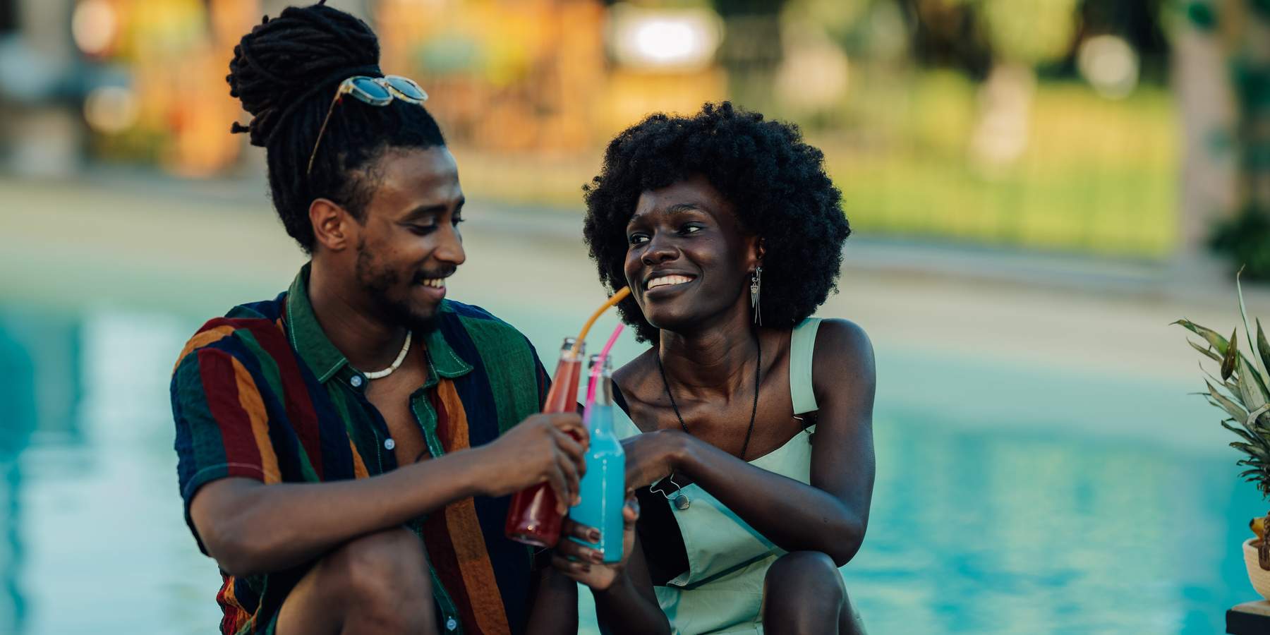 Young couple toasting with colorful beverages, enjoying a relaxing moment by the pool during summer vacation, celebrating their love and togetherness in a vibrant and refreshing setting