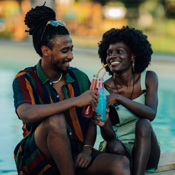 Young couple toasting with colorful beverages, enjoying a relaxing moment by the pool during summer vacation, celebrating their love and togetherness in a vibrant and refreshing setting