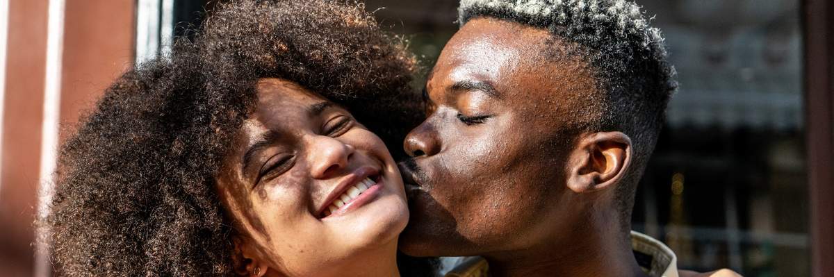 Young-man-kissing-girlfriend-on-the-cheek-outdoors