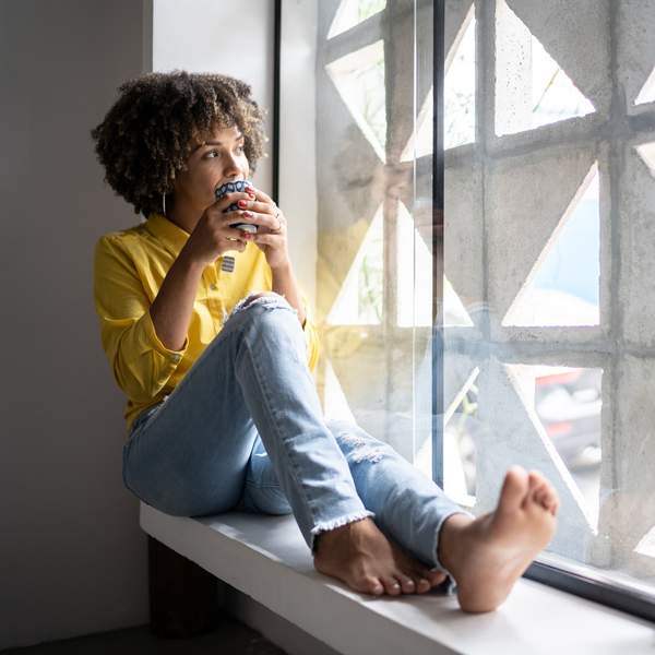 young-woman-curly-hair-drinking-warm-beverage-sitting-on-window-sill