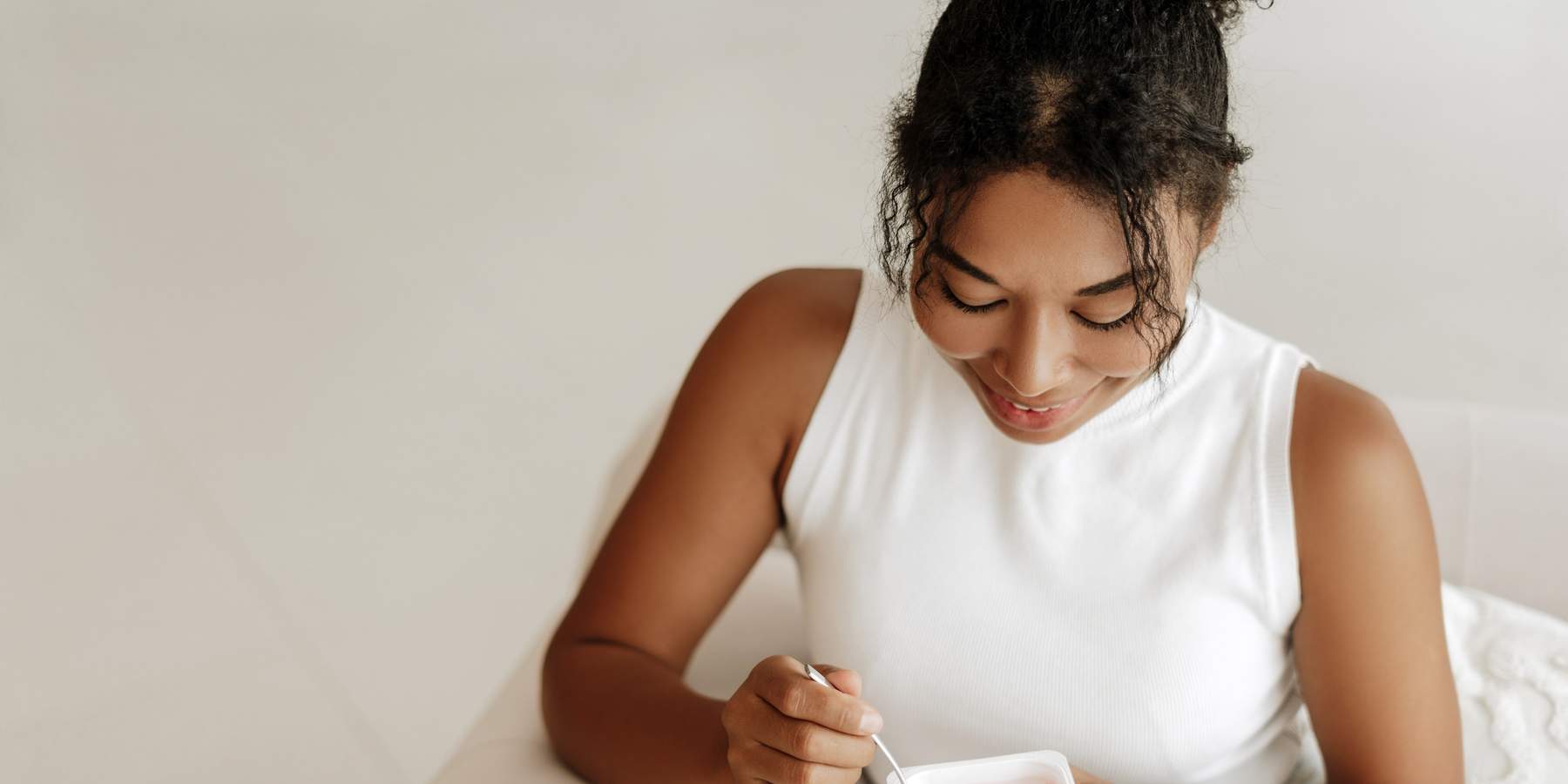 Young woman smiling while eating yogurt at home, symbolizing probiotics and vaginal health for preventing yeast infections after sex.