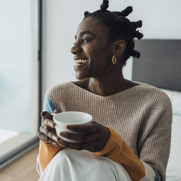 young-woman-smiling-with-afro-hairstyle-sitting-on-bed-and-drinking-coffee