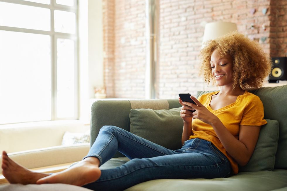 young-woman-with-curly-hair-smiling-at-her-phone-sitting-on-the-couch-at-home