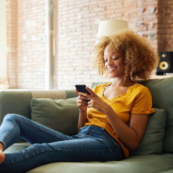 young-woman-with-curly-hair-smiling-at-her-phone-sitting-on-the-couch-at-home